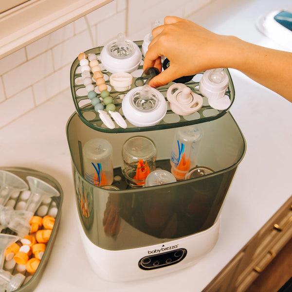 a hand lifting the top rack of the Baby Brezza SDA filled with parts and bottles - product thumbnail